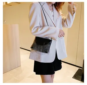 Detail of black leather crossbody bag with metal ring and tassel chain on beige blazer