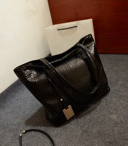 Détail du cabas noir à motif crocodile brillant avec pendentif métallique élégant