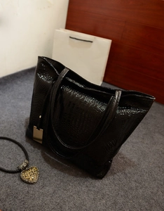 Détail d'un sac cabas noir à motif crocodile brillant avec pendentif métallique poli