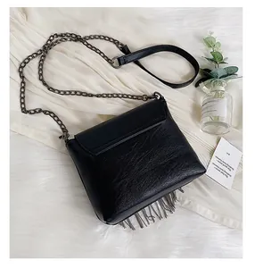 Detail of black leather crossbody bag with metallic tassels and dark silver chain strap