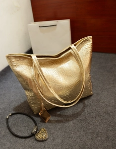 Détail du sac cabas doré avec texture crocodile et collier à pendentif cœur décoratif