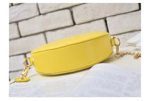 Detail view of yellow circular orange crossbody bag with gold chain strap on table