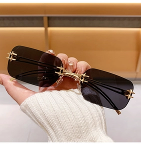 Close-up of rimless sunglasses with gold cross metal hinges and dark gradient lenses