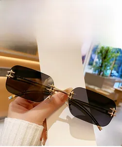 Detail of bright gold cross-shaped metal bridge on rimless rectangle sunglasses with grey lenses