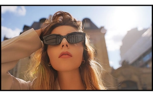 Chic low-angle shot of a model wearing retro thick black rectangular sunglasses outdoors