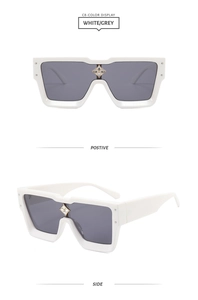 Detail of white wide-frame sunglasses featuring a floral metal emblem on the bridge