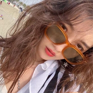 Chic orange transparent square sunglasses with dark lenses worn by a model on a beach