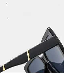 Close-up of black oversized sunglasses with parallel gold metal bars on wide temples