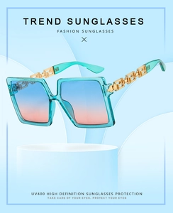 Detail of mint green square sunglasses featuring golden Greek Key pattern on metal temples