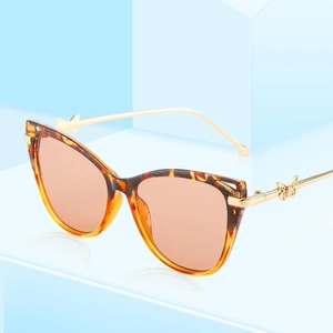 Cat eye tortoiseshell sunglasses with golden butterfly metal temples on a blue stand
