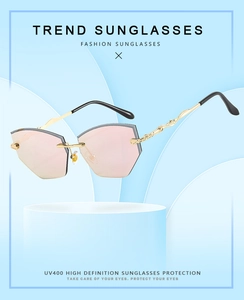 Close-up of rimless hexagonal sunglasses with pink lenses and engraved gold temples
