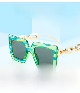 Detail of square sunglasses with blue-green stripes and gold metal chain temples