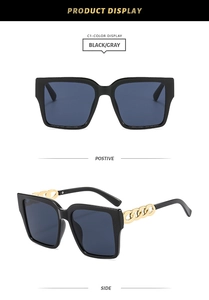 Detail view of square black sunglasses with chunky gold chain temples and grey lenses
