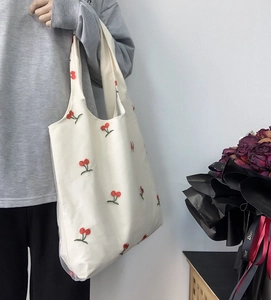 Detail of red cherry embroidery on white canvas tote bag with textured mesh overlay