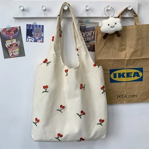 Detail shot of small cherry embroidery on off-white canvas tote bag hanging on a hook