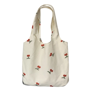 White canvas tote bag with delicate red cherry embroidery and integrated dual handles