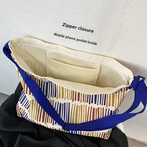 Detail of striped canvas crossbody bag featuring a top zipper and internal phone pocket