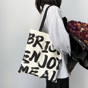 Detailed side view of white canvas tote bag with black lettering held by model with flowers