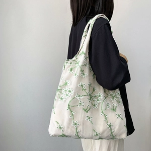 Detail of floral embroidery on off-white mesh lace canvas tote bag worn by a model
