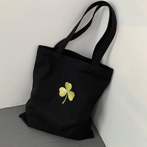 Detail of yellow shamrock embroidery on a black canvas tote bag for school or daily use
