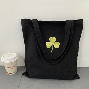 Detail of green clover embroidery on a black canvas tote bag with a minimalist design