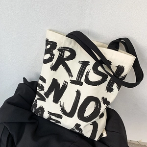 Minimalist canvas tote bag with bold black artistic lettering and wide shoulder straps