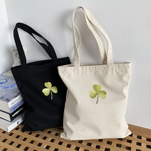 Close-up of green clover embroidery details on black and beige canvas tote bags