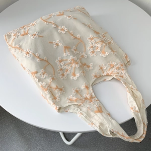 Detail of floral embroidery on off-white mesh tote bag with orange daisy pattern