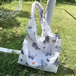Detail view of the white frayed fabric texture and orange butterfly print on the tote bag