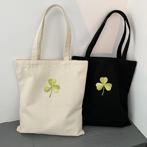 Detail of green clover embroidery on black and white canvas tote bags with long handles