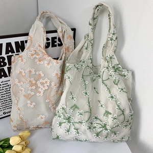 Detail of daisy flower embroidery on translucent white mesh tote bags in two colors