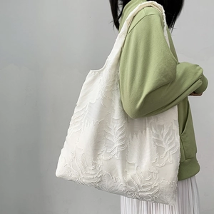 White textured tote bag with leaf embroidery carried by model in casual green outfit