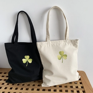 Classic clover embroidery canvas tote bags in black and white colors on a wooden bench