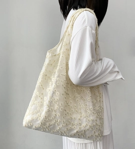 Detail of delicate daisy embroidery on a semi-transparent ivory mesh tote bag