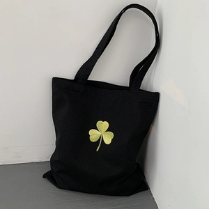 Detailed close-up of lucky clover embroidery on black canvas tote bag surface