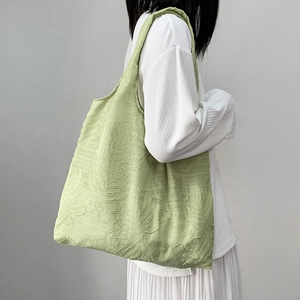 Light green tote bag with leaf jacquard texture shown on a shoulder in a casual style
