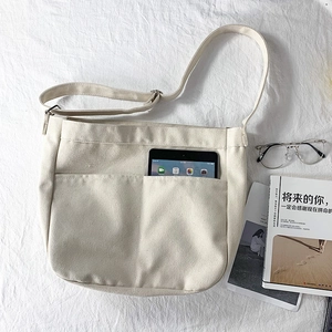 Detail of beige canvas crossbody bag with front pocket showing space for a tablet