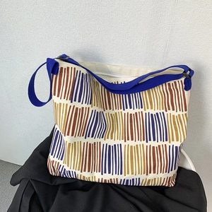 Close-up of a large canvas tote bag showing abstract stripes and blue shoulder strap