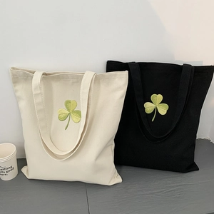 Detailed view of black and cream canvas tote bags with green clover embroidery and handles