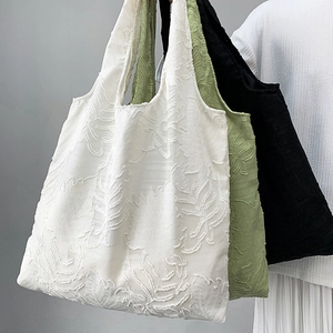 Detail shot of the textured tote bag showing 3D floral leaf embroidery in white and green