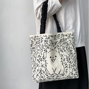Detail view of the black ruffled handle and cartoon dog print on the canvas tote bag