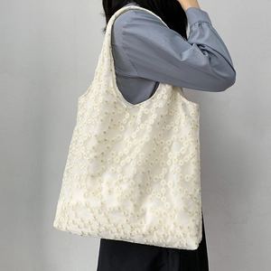Detail of white canvas tote bag featuring delicate daisy embroidery and mesh fabric texture
