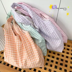 Detail of four colorful gingham seersucker tote bags in pastel tones on a wooden bench