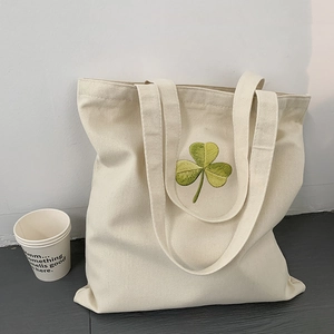 Close-up of green clover embroidery on off-white canvas tote bag with reinforced handles