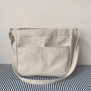 Close-up of beige canvas crossbody bag with two front pockets and adjustable strap