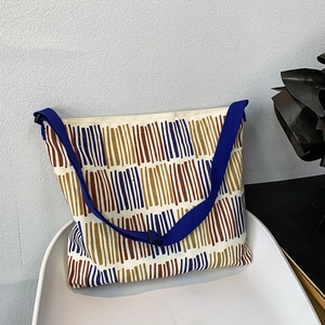 Detail of artistic striped canvas bag with adjustable wide strap on a white chair