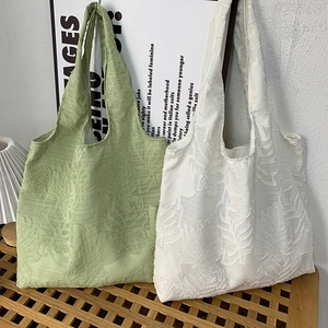 Detailed view of two jacquard tote bags with textured leaf patterns on a wooden stool