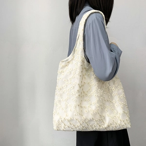 Detailed view of white floral lace tote bag with daisy embroidery on model's shoulder