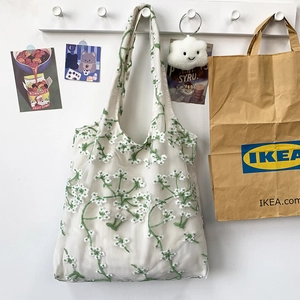 Detail of white mesh lace tote bag with green botanical embroidery hanging on a hook