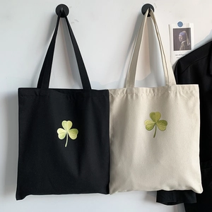 Detailed close-up of green shamrock embroidery on black and beige canvas tote bags